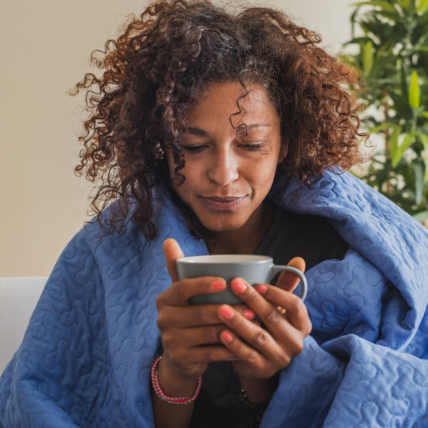 woman wrapped in a blanket clasping a cup of hot liquid