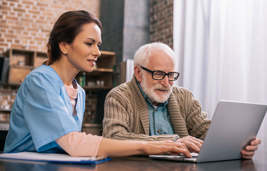 a nurse assisting an elderly man using a laptop